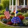 Red white blue patriotic porch goose outfit placed in flower garden beside American flag for 4th of July decor
