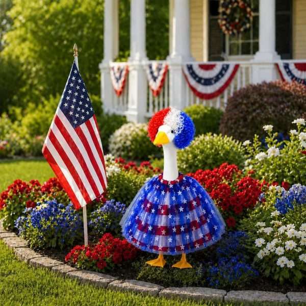 Red white blue patriotic porch goose outfit placed in flower garden beside American flag for 4th of July decor