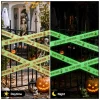 Daytime and night view of glow Halloween caution tape crossed over an iron gate with pumpkins, skeleton and ghosts