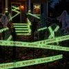 Night view of a house with glowing Halloween caution tape across the windows, front door and lawn with skeletons and ghosts