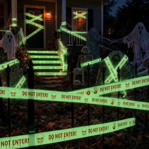 Night view of a house with glowing Halloween caution tape across the windows, front door and lawn with skeletons and ghosts