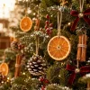 Close-up of the ornaments on a lit tree – orange slice, cinnamon bundle, pinecone, red berries and a velvet bow with bell hanging from jute twine