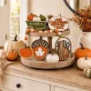 Fall wooden signs and bead garland on a tiered tray on a sideboard with pumpkins and a round mirror