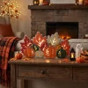 Lighted fall pumpkin decoration on a console table in front of a fireplace with a lantern and mini pumpkins
