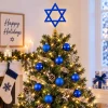Christmas tree with a blue Star of David topper in a white living room with a Happy Holidays sign and a blue stocking