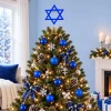 Decorated tree with the blue Star of David topper beside a fireplace with garland and candles and wrapped gifts
