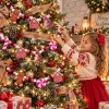 Girl decorating a Christmas tree wrapped with the pink gingerbread pom garland