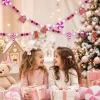 Two girls with wrapped gifts in a pink Christmas room, the gingerbread garland hung across the wall above them