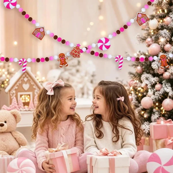 Two girls with wrapped gifts in a pink Christmas room, the gingerbread garland hung across the wall above them
