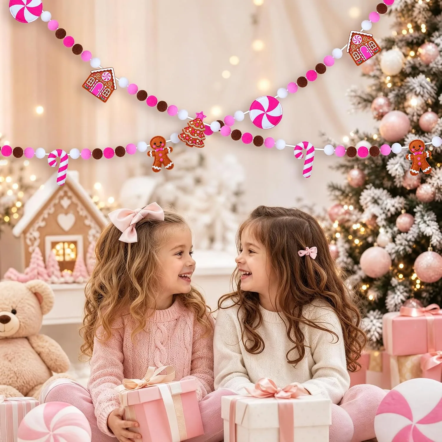 Two girls with wrapped gifts in a pink Christmas room, the gingerbread garland hung across the wall above them