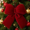 The 13 inch red velvet bow hanging on a lit Christmas tree among red and gold baubles